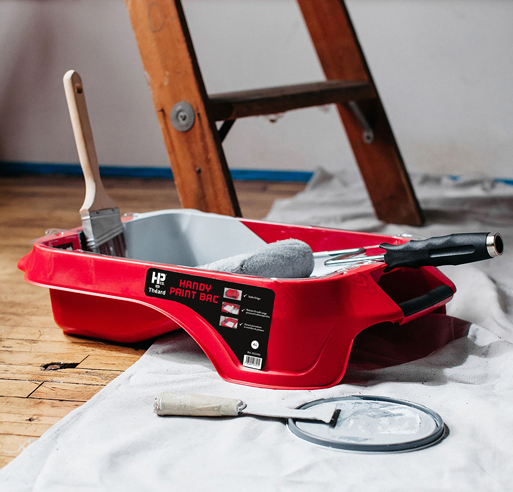 Image d'un bac de peinture handy paint avec un pinceau, un rouleau et un riflard sur un chantier